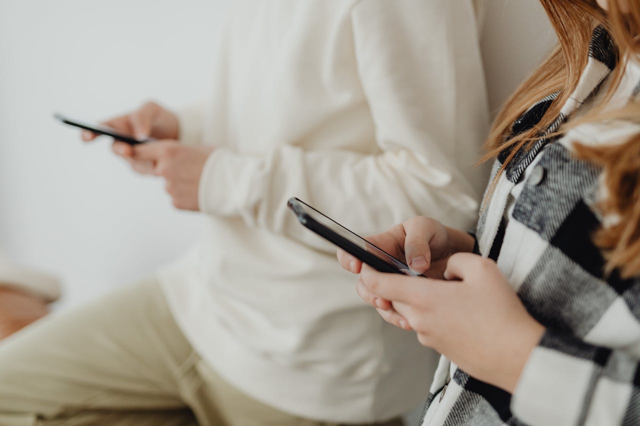 Close-up of two people using smartphones indoors, highlighting technology and communication.